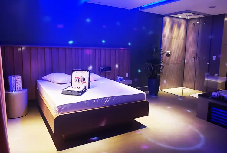 Cama confortável com cabeceira de madeira e iluminação azul relaxante com vista para a ducha envidraçada