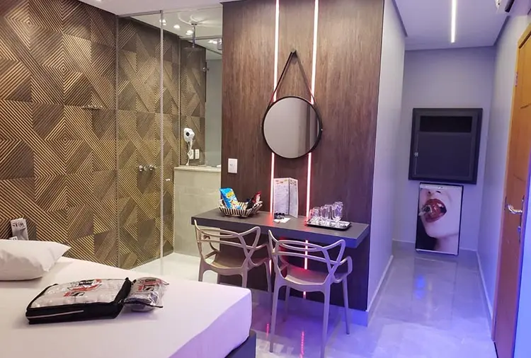 Bancada de apoio com espelho de LED neon, cadeiras de design e frigobar na Suíte Júpiter