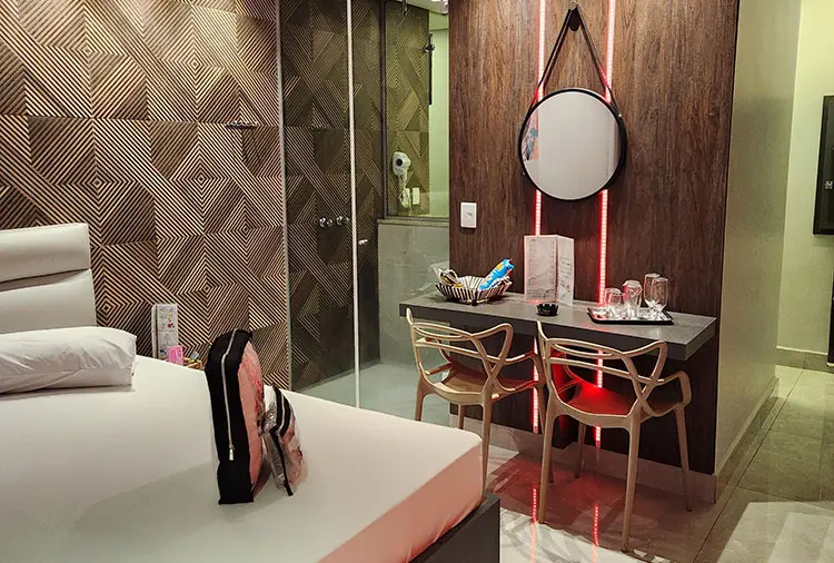 Bancada moderna da Suíte Órion com cadeiras de design, espelho com neon vermelho e taças