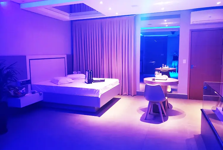 Quarto amplo com cama espaçosa, mesa com cadeiras de design e iluminação violeta sob teto rebaixado na Suíte Star