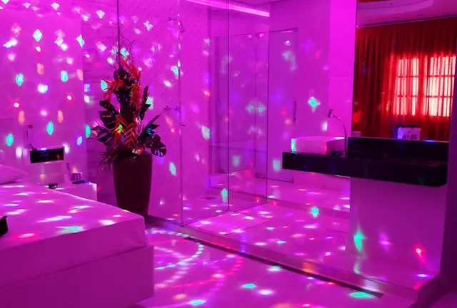 Visão panorâmica da Suíte Vênus com banheira de hidromassagem envidraçada sob luz magenta